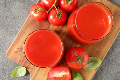 Photo of Tasty tomato juice in glasses, basil and fresh vegetables on grey table, top view