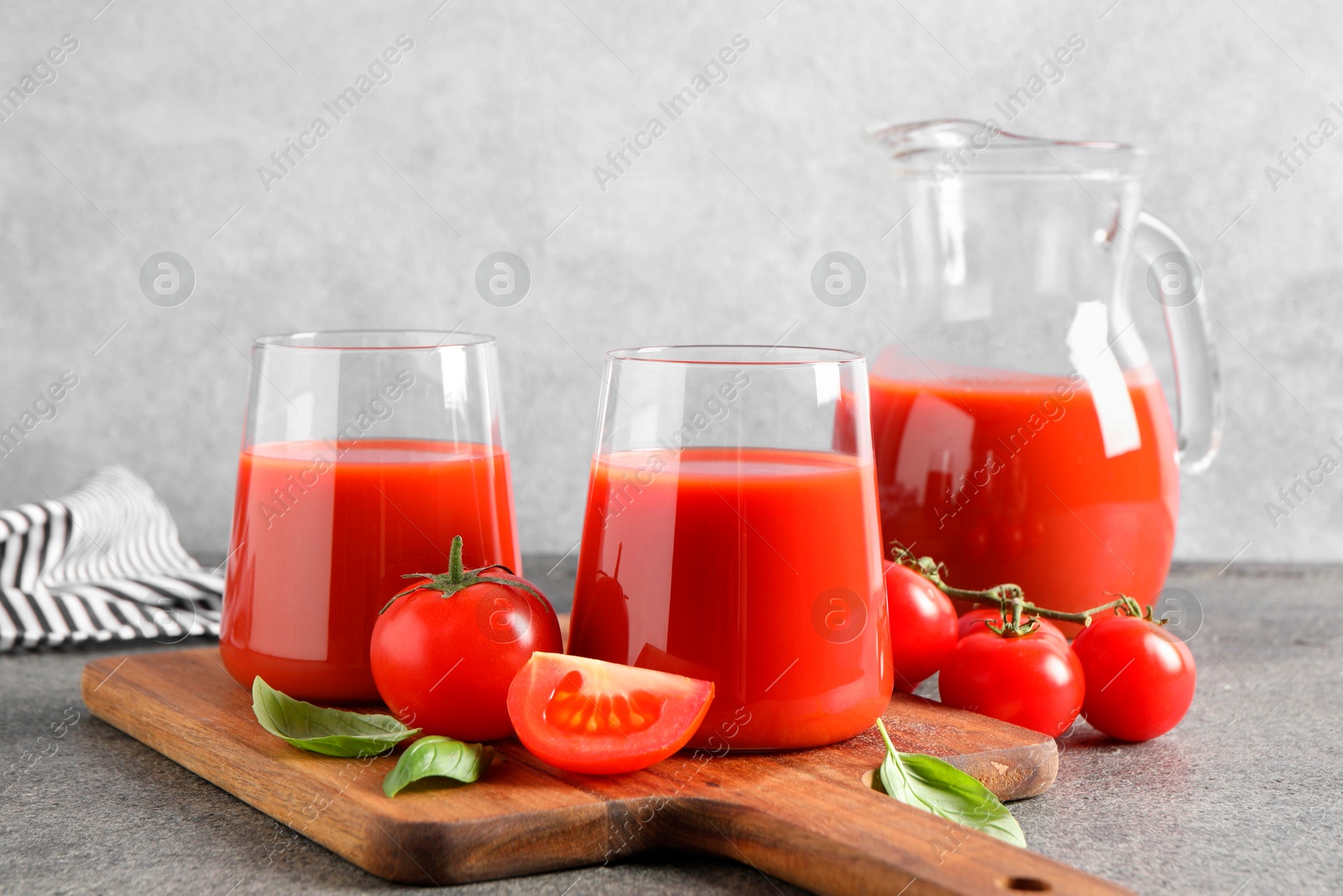 Photo of Tasty tomato juice in glasses, basil and fresh vegetables on grey table