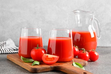 Tasty tomato juice in glasses, basil and fresh vegetables on grey table