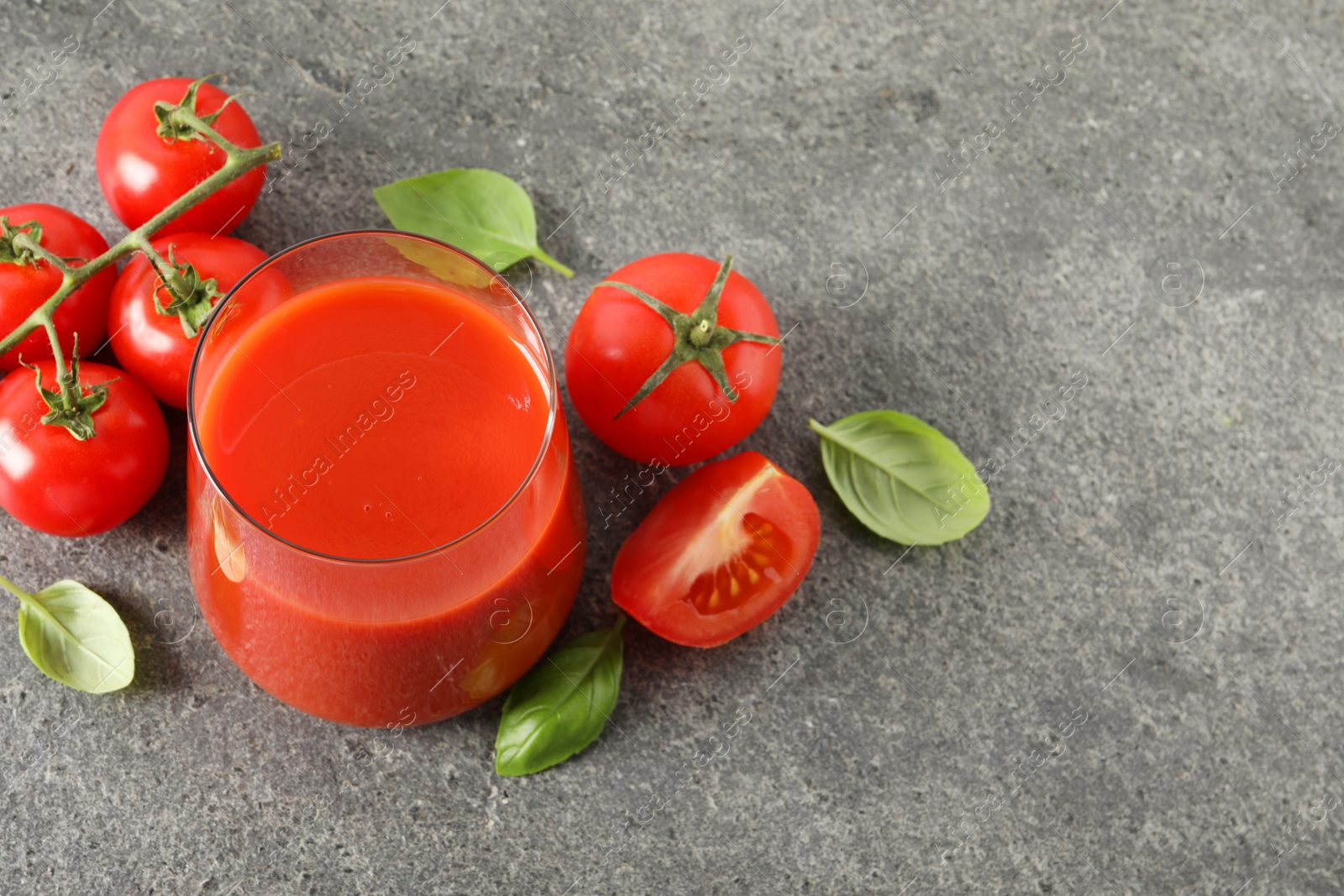 Photo of Tasty tomato juice in glass, basil and fresh vegetables on grey table, above view. Space for text