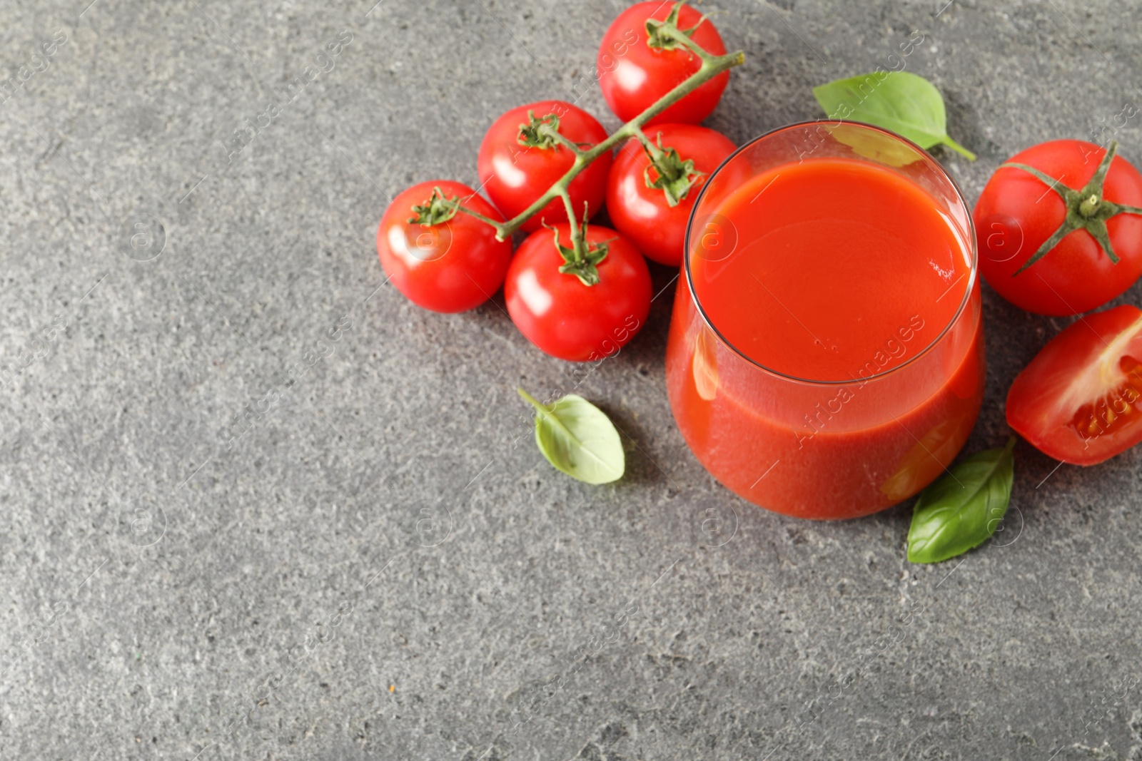 Photo of Tasty tomato juice in glass, basil and fresh vegetables on grey table, above view. Space for text