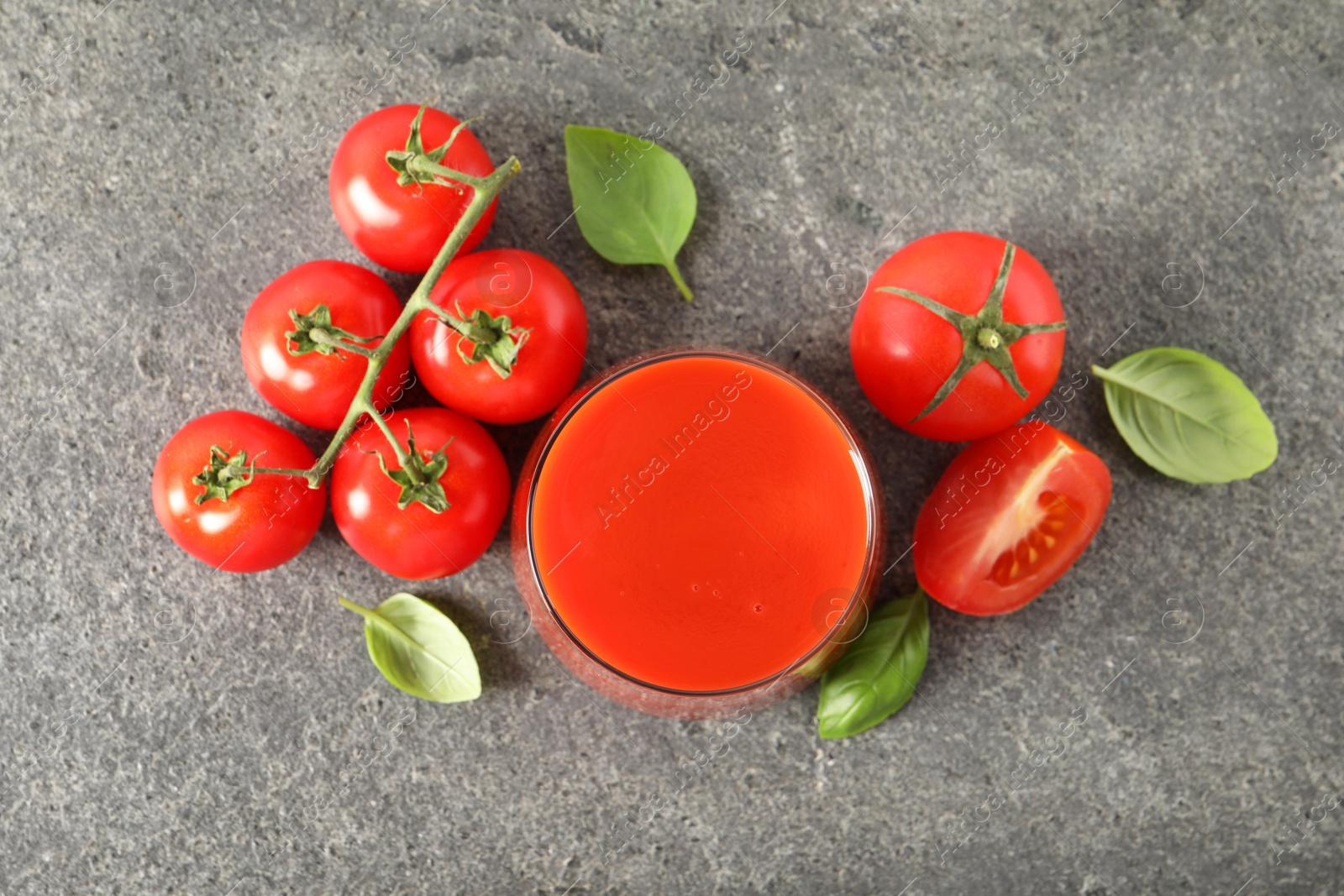 Photo of Tasty tomato juice in glass, basil and fresh vegetables on grey table, flat lay