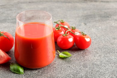 Tasty tomato juice in glass, basil and fresh vegetables on grey table. Space for text