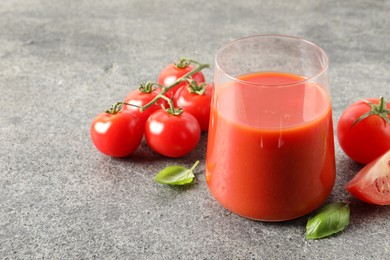 Photo of Tasty tomato juice in glass, basil and fresh vegetables on grey table. Space for text