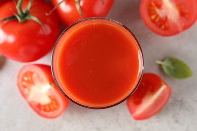 Tasty tomato juice in glass, basil and fresh vegetables on light grey table, top view