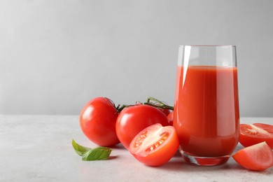 Tasty tomato juice in glass, basil leaves and fresh vegetables on light grey table. Space for text