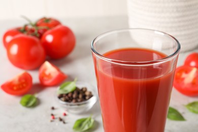 Photo of Tasty tomato juice in glass, basil leaves and fresh vegetables on table, closeup