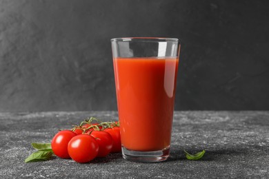 Tasty tomato juice in glass, basil and fresh vegetables on grey table