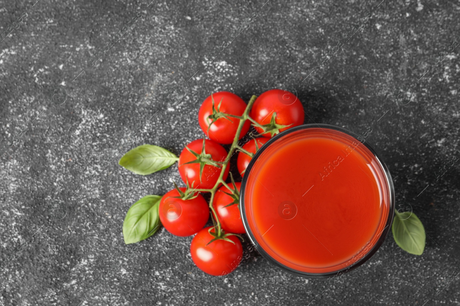 Photo of Tasty tomato juice in glass, basil and fresh vegetables on grey table, top view