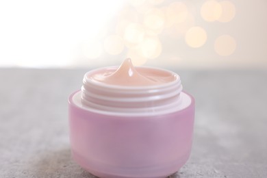 Photo of Jar of cream on gray table against light background with blurred lights, closeup