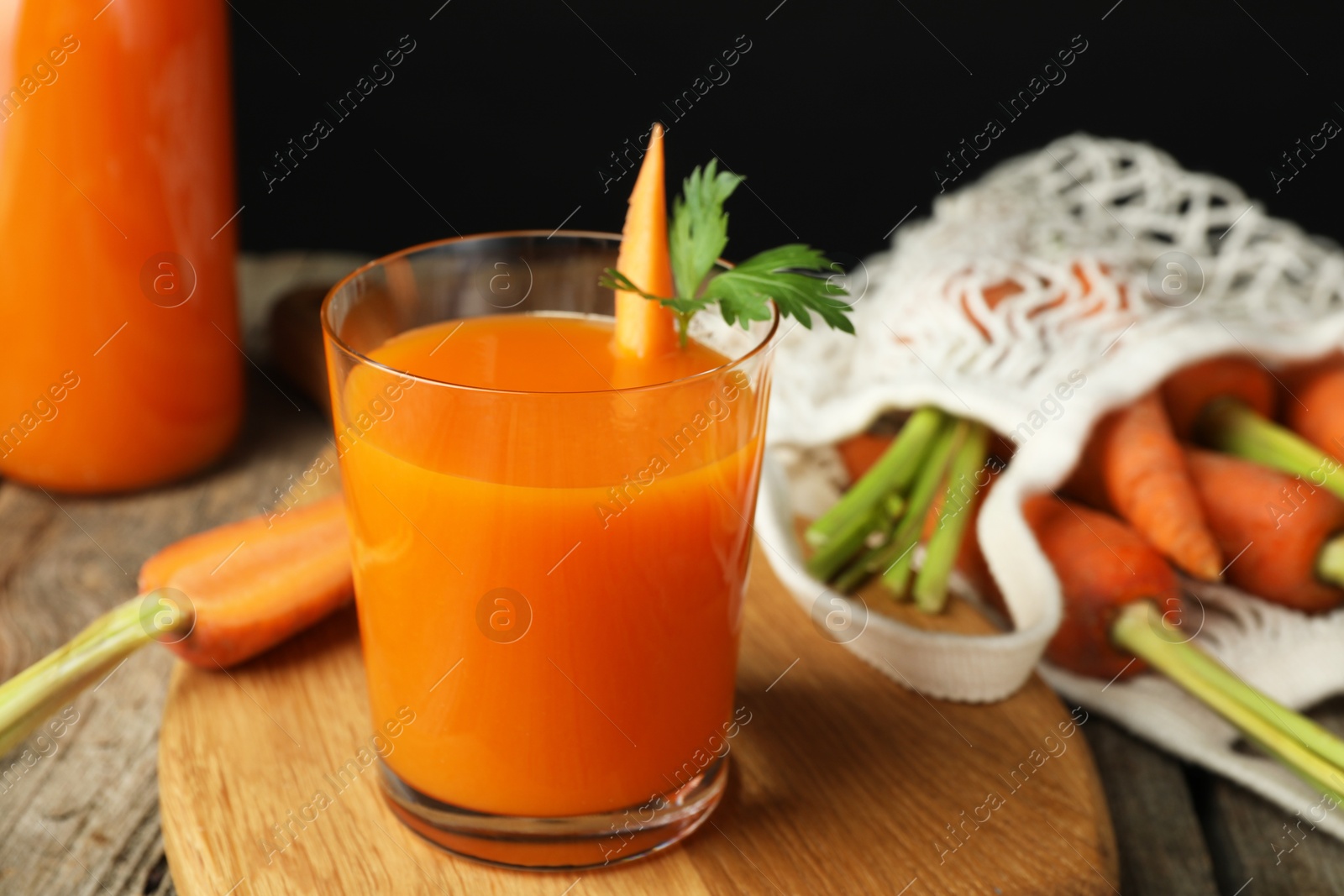 Photo of Healthy juice in glass and fresh carrot on wooden table