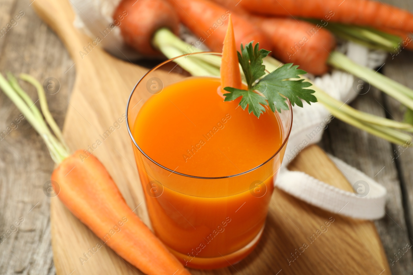 Photo of Healthy juice in glass and fresh carrot on wooden table, closeup