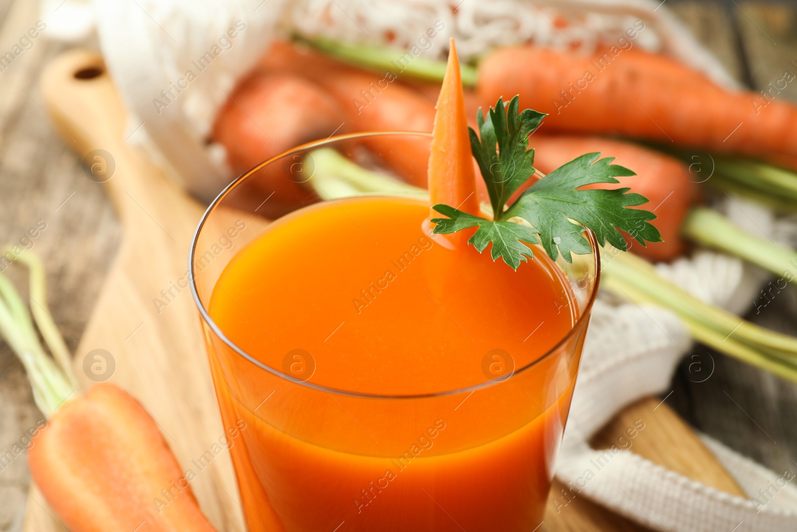 Photo of Healthy juice in glass and fresh carrot on wooden table, closeup