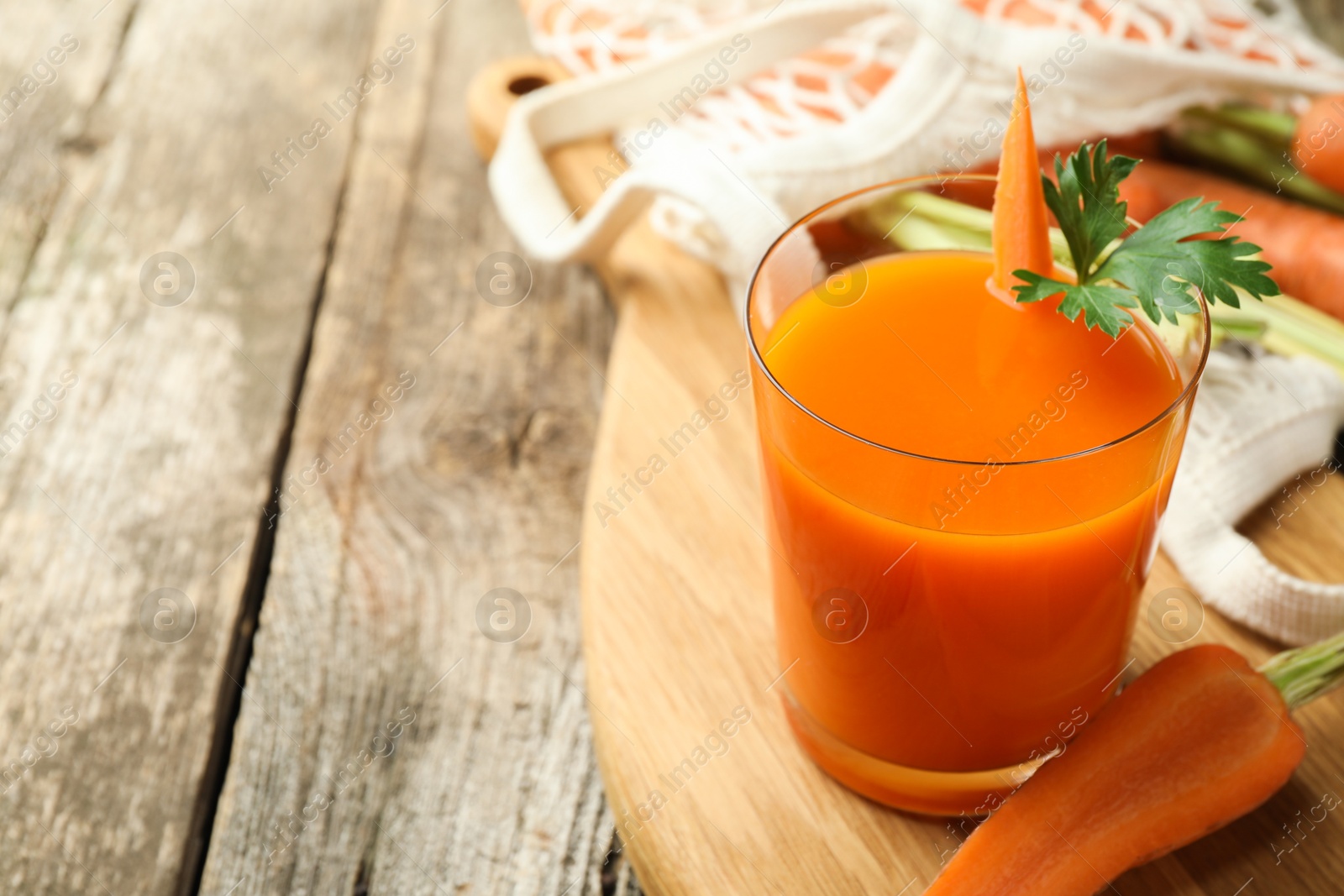 Photo of Healthy juice in glass and fresh carrot on wooden table. Space for text