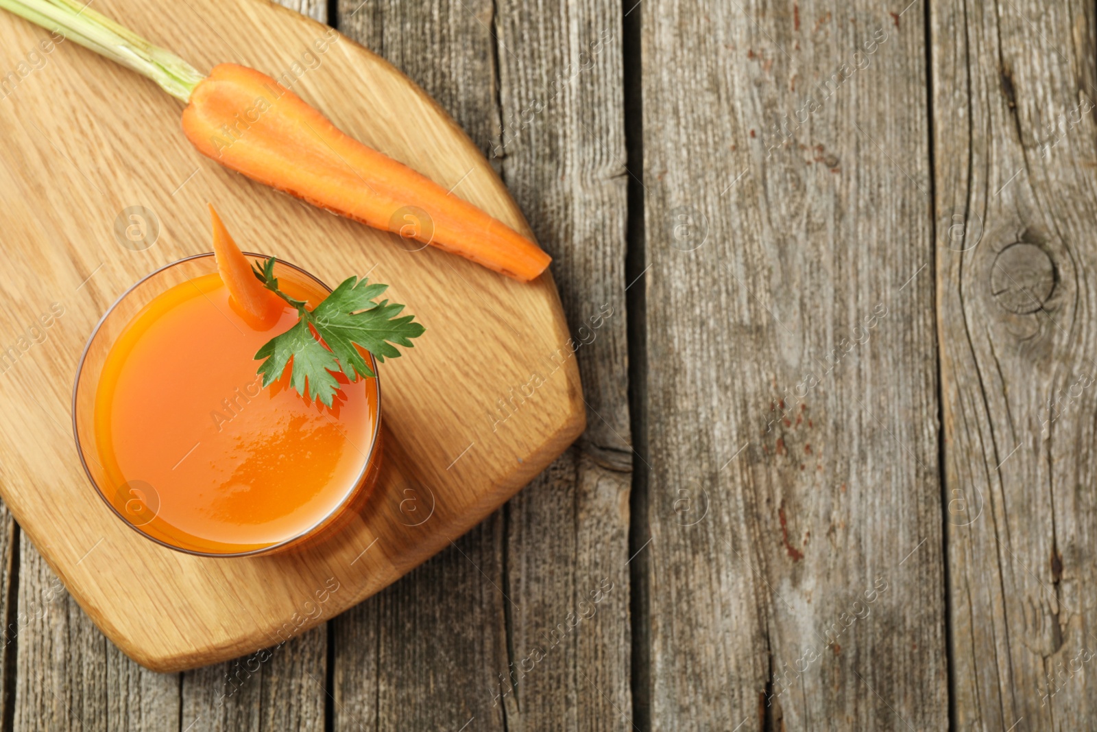 Photo of Healthy juice in glass and fresh carrot on wooden table, top view. Space for text