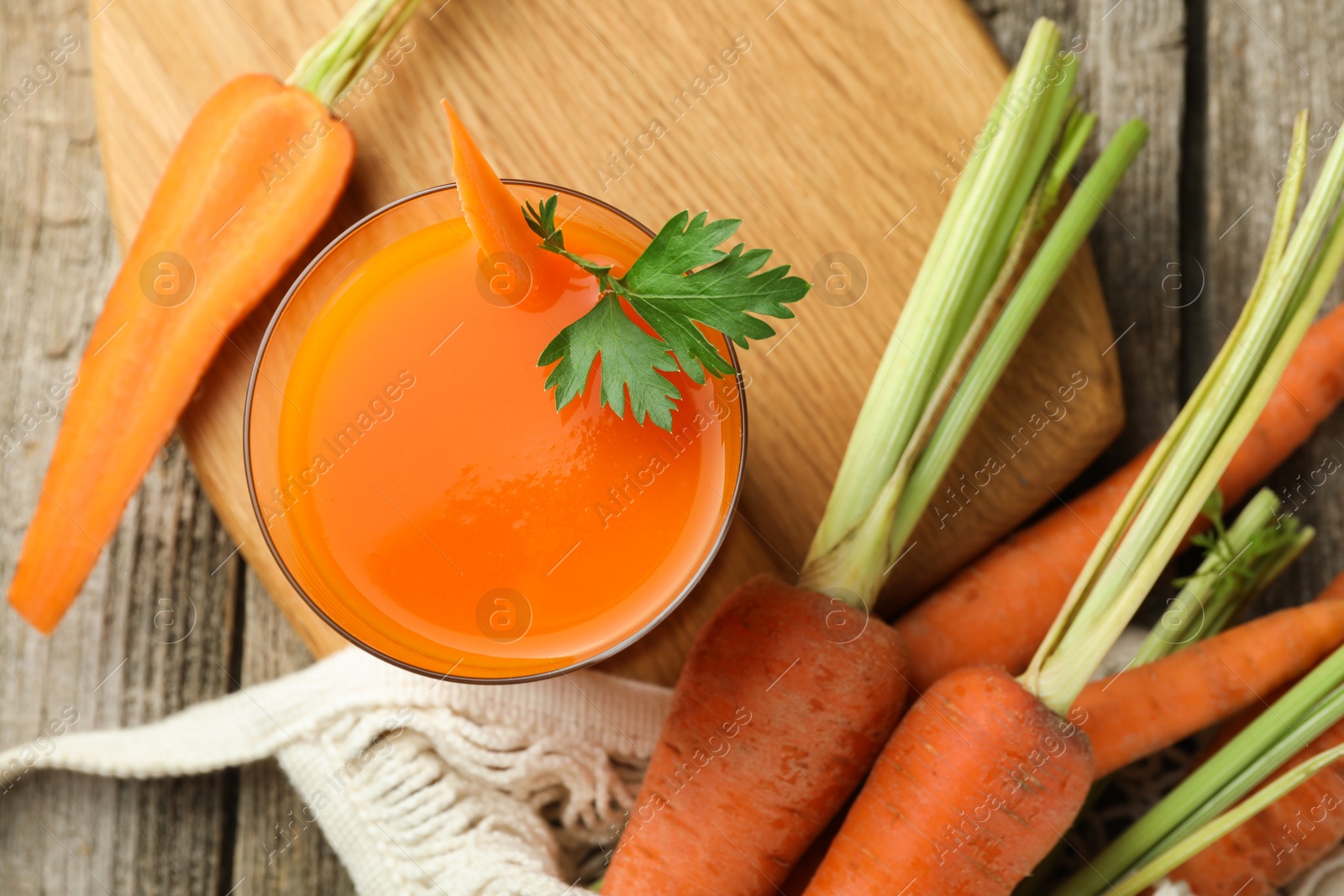 Photo of Healthy juice in glass and fresh carrot on wooden table, flat lay