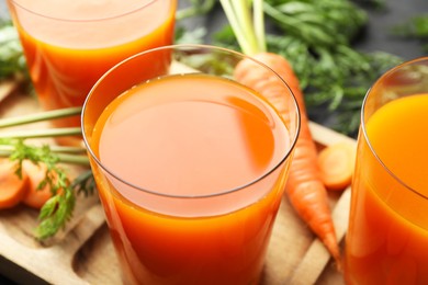 Photo of Healthy carrot juice in glasses and fresh vegetable on table, closeup