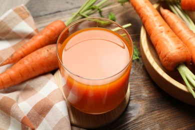 Photo of Healthy carrot juice in glass and fresh vegetables on wooden table