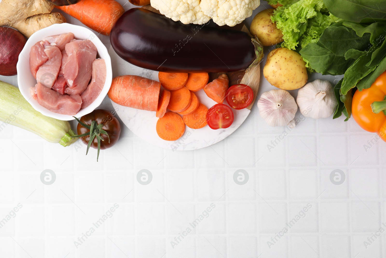 Photo of Different vegetables and raw meat for stew on white tiled table, top view. Space for text