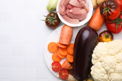 Photo of Different vegetables and raw meat for stew on white tiled table, top view. Space for text