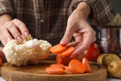 Cooking vegetable stew. Woman with cut carrot and cauliflower at table, closeup