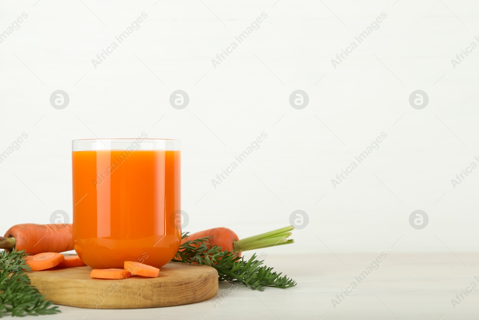 Photo of Fresh carrot juice in glass and vegetables on light wooden table against white background. Space for text