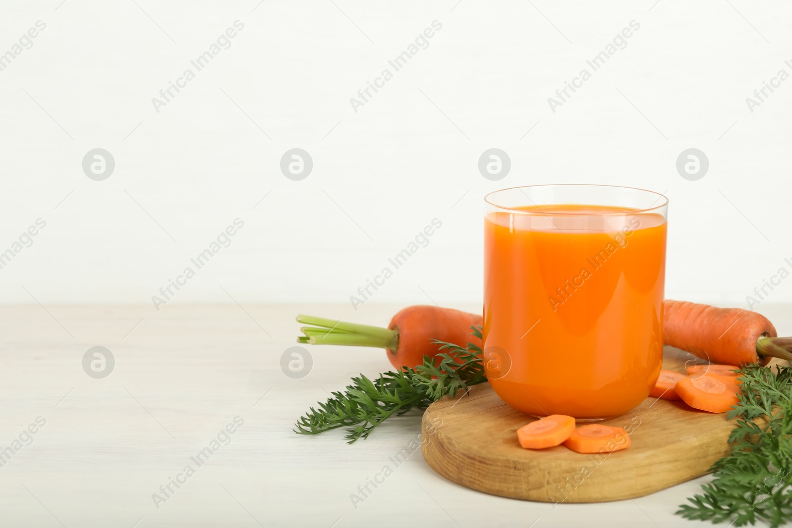 Photo of Fresh carrot juice in glass and vegetables on light wooden table against white background. Space for text