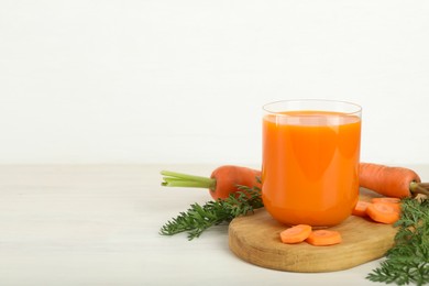 Fresh carrot juice in glass and vegetables on light wooden table against white background. Space for text