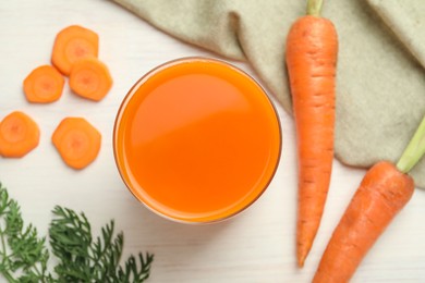 Fresh carrot juice in glass and vegetables on light wooden table, flat lay