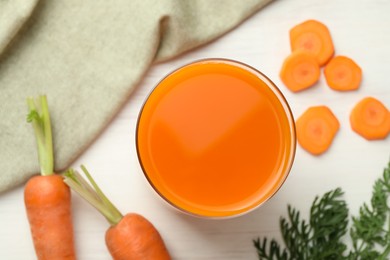 Fresh carrot juice in glass and vegetables on light wooden table, flat lay