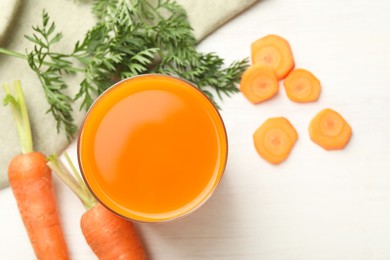 Fresh carrot juice in glass and vegetables on light wooden table, flat lay