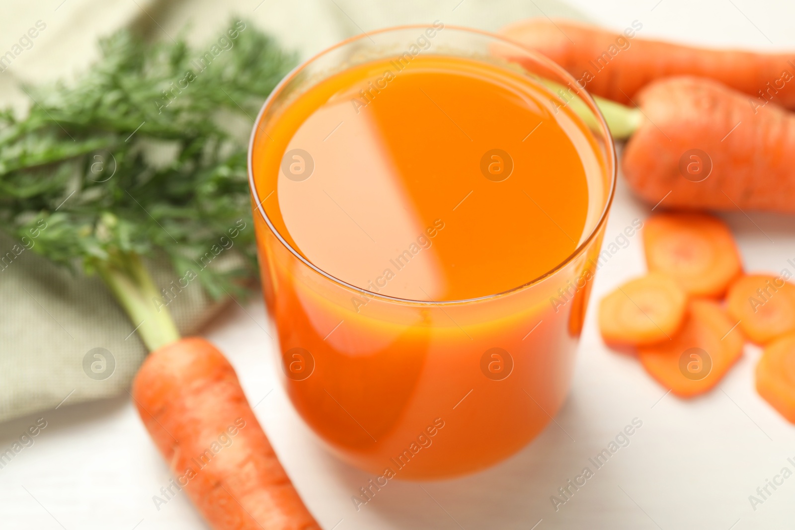 Photo of Fresh carrot juice in glass and vegetables on light table, closeup