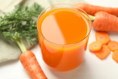 Photo of Fresh carrot juice in glass and vegetables on light table, closeup