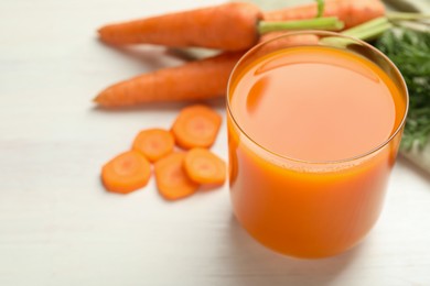 Photo of Fresh carrot juice in glass and vegetables on light wooden table, closeup. Space for text