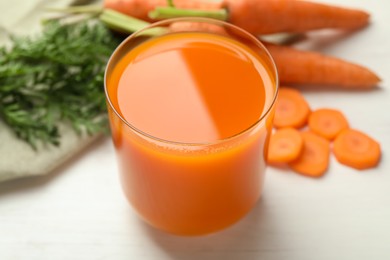 Fresh carrot juice in glass and vegetables on light table, closeup