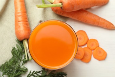 Fresh carrot juice in glass and vegetables on light table, flat lay