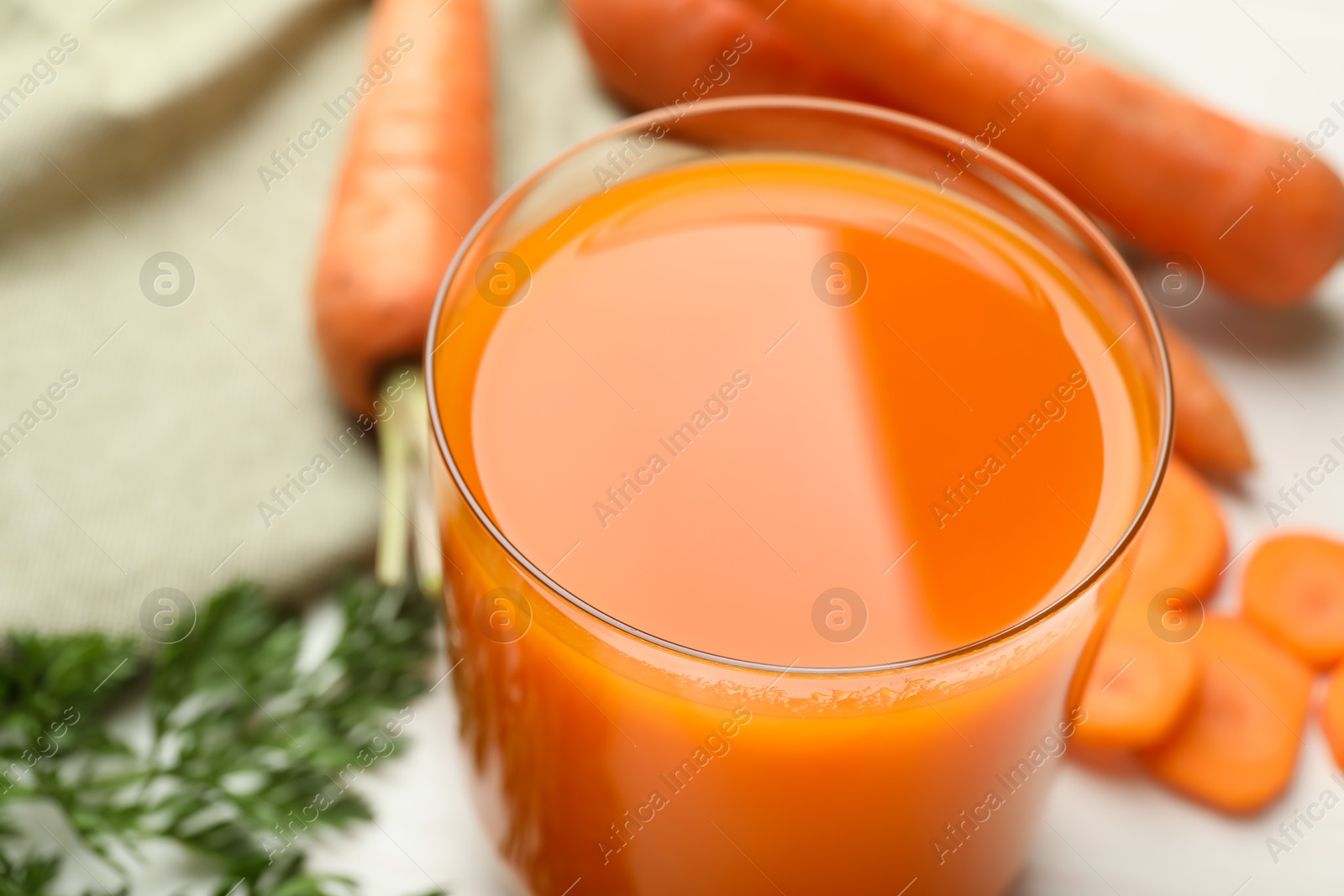 Photo of Fresh carrot juice in glass and vegetables on light table, closeup