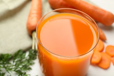 Photo of Fresh carrot juice in glass and vegetables on light table, closeup