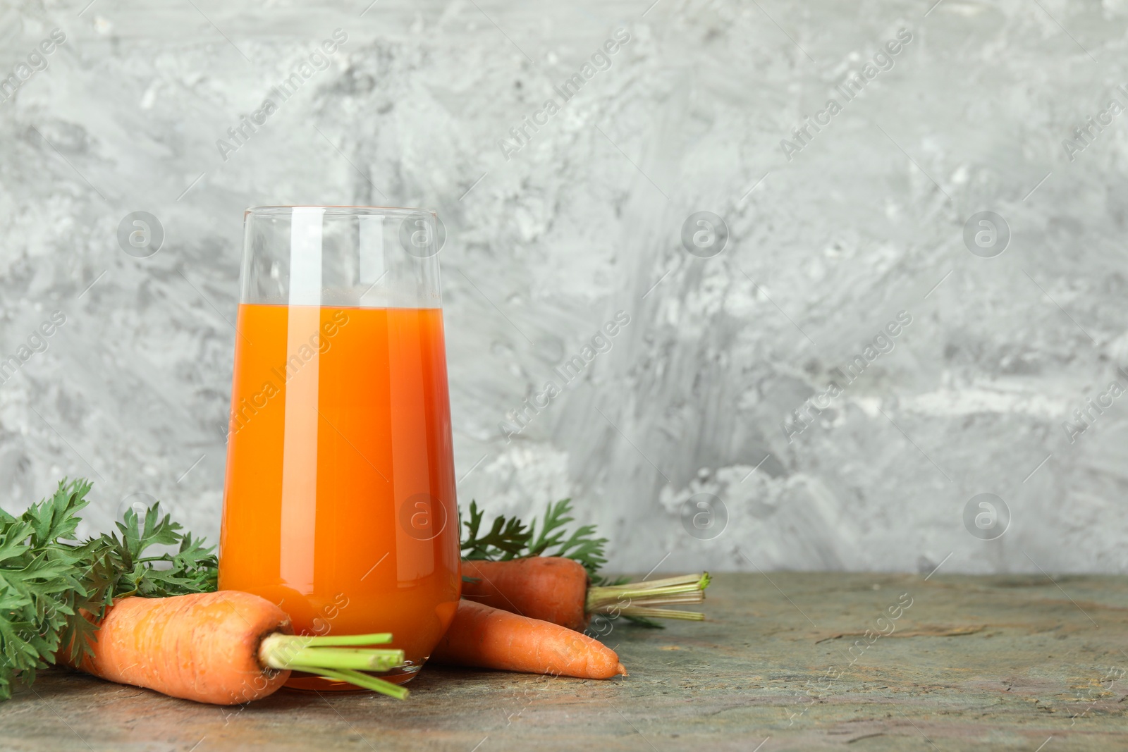 Photo of Fresh carrot juice in glass and vegetables on textured table. Space for text