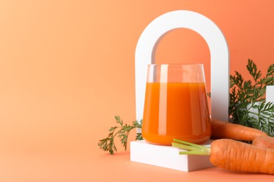 Photo of Fresh carrot juice in glass and vegetables on coral background, closeup. Space for text