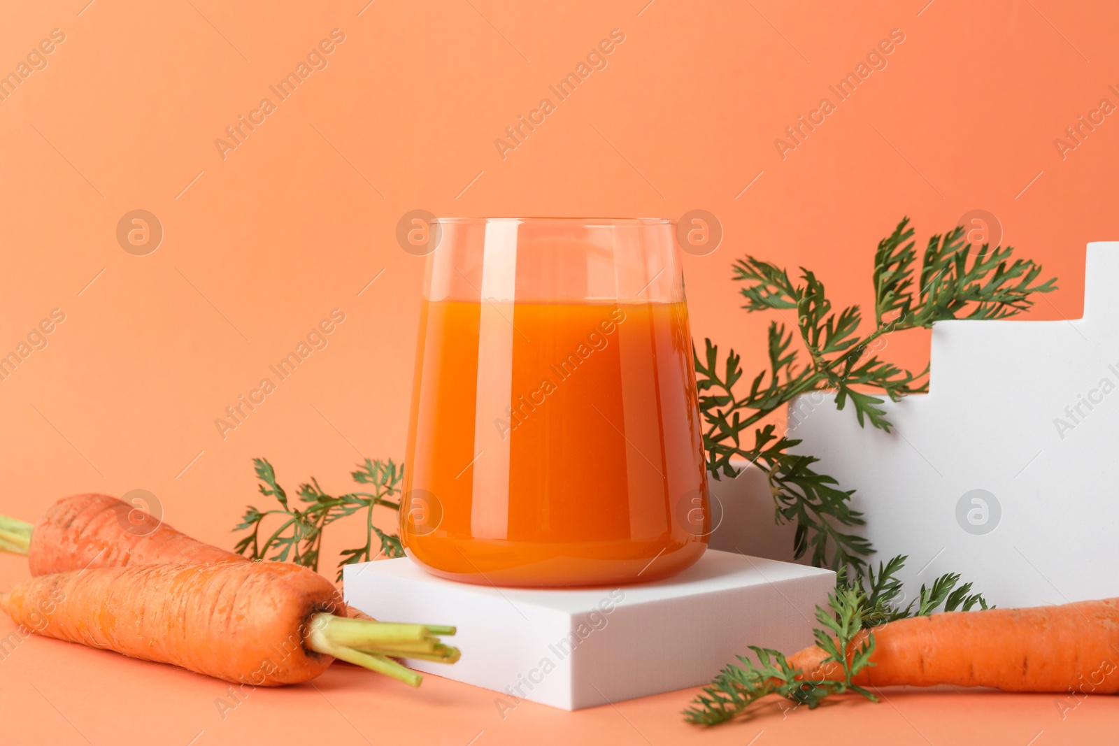 Photo of Fresh carrot juice in glass and vegetables on coral background, closeup