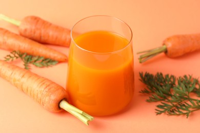 Fresh carrot juice in glass and vegetables on coral background, closeup