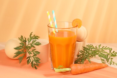 Fresh carrot juice in glass and vegetable on coral background