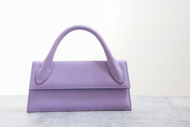 Photo of Stylish violet bag on gray table against light background, space for text