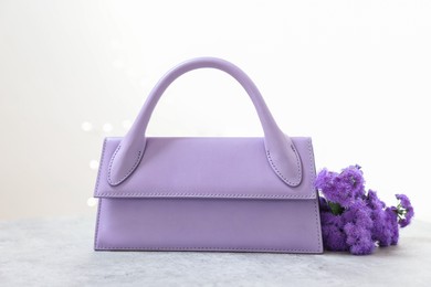 Photo of Stylish violet bag and ageratum flowers on gray table against light background