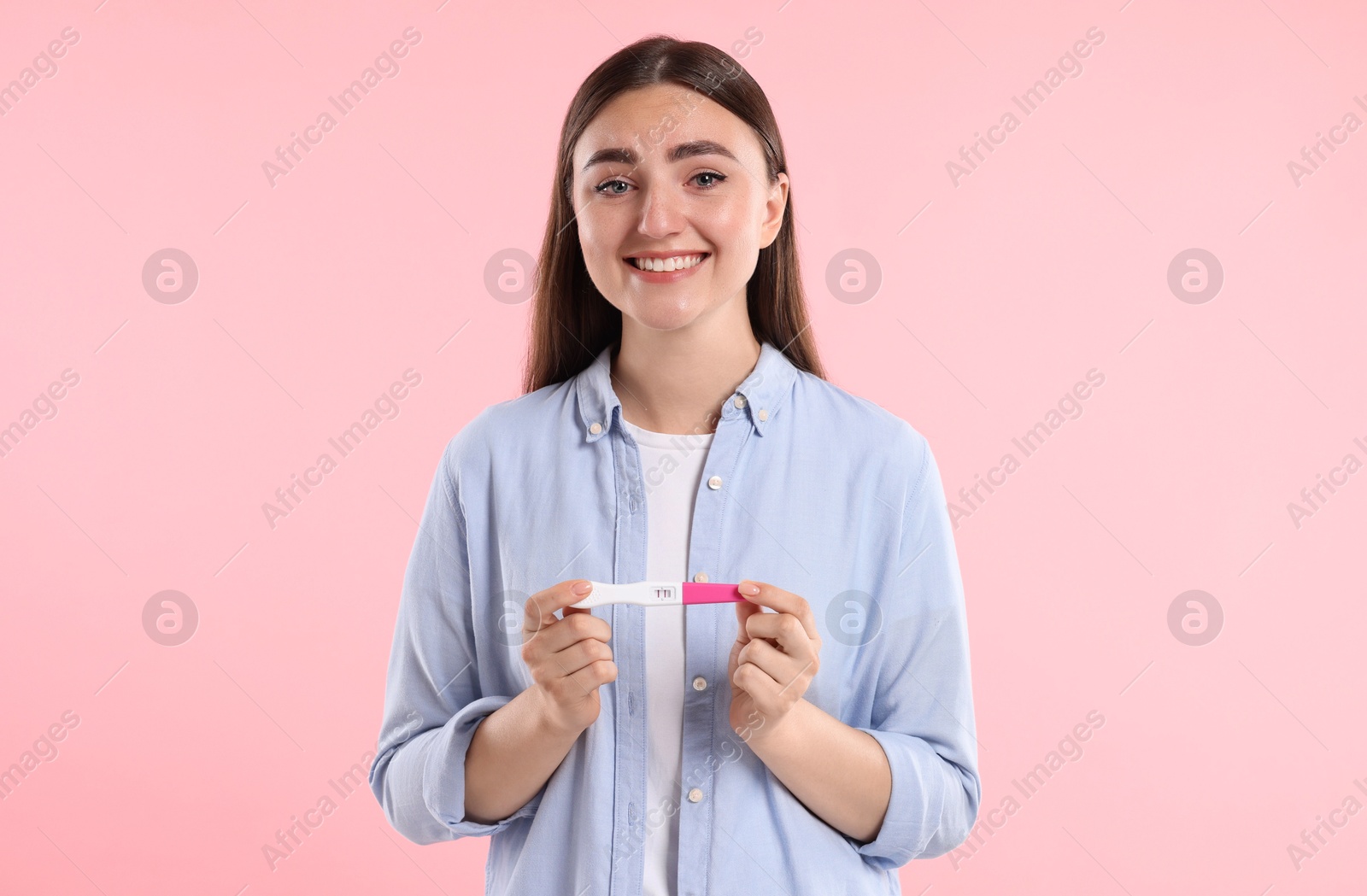 Photo of Happy woman holding pregnancy test on pink background