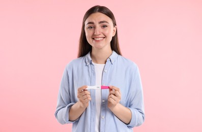 Happy woman holding pregnancy test on pink background