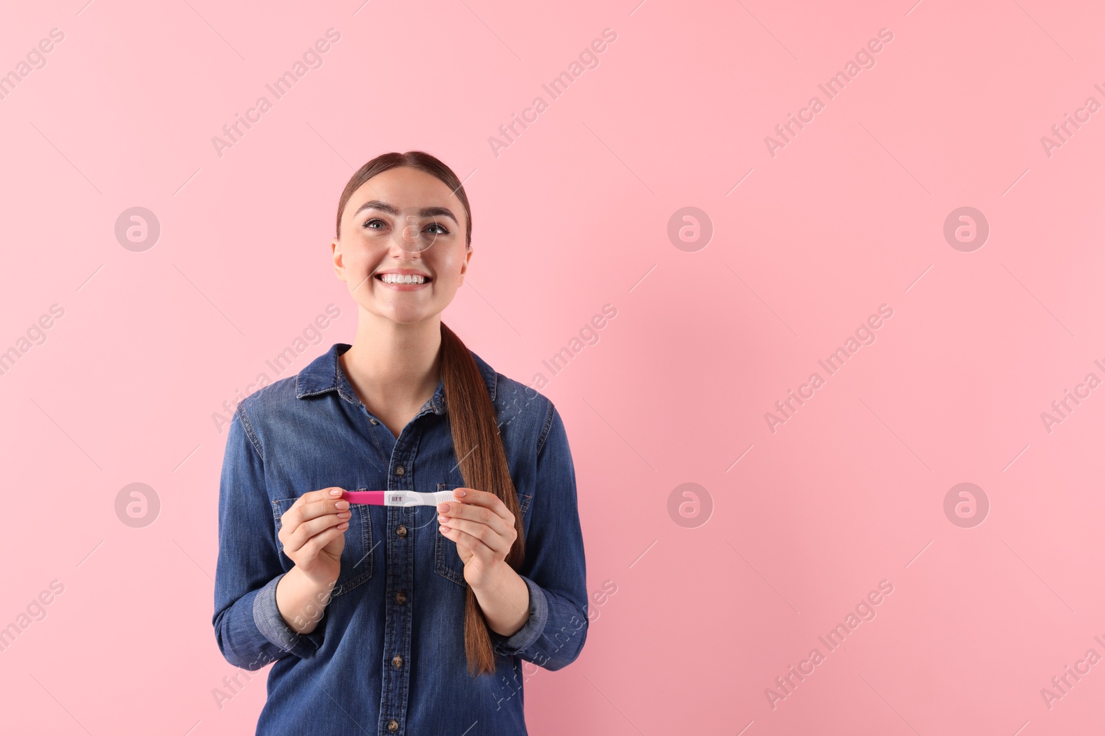 Photo of Happy woman holding pregnancy test on pink background, space for text