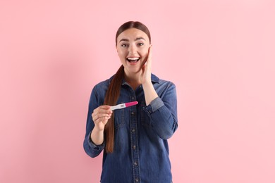 Photo of Happy woman holding pregnancy test on pink background