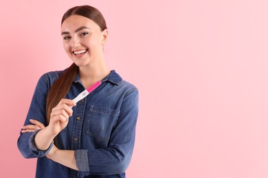 Photo of Happy woman holding pregnancy test on pink background, space for text